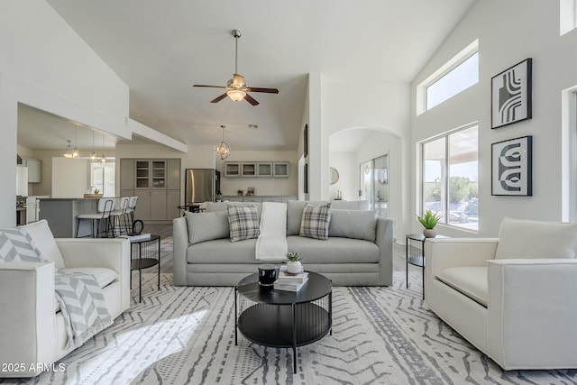 living room featuring arched walkways, plenty of natural light, ceiling fan with notable chandelier, and high vaulted ceiling