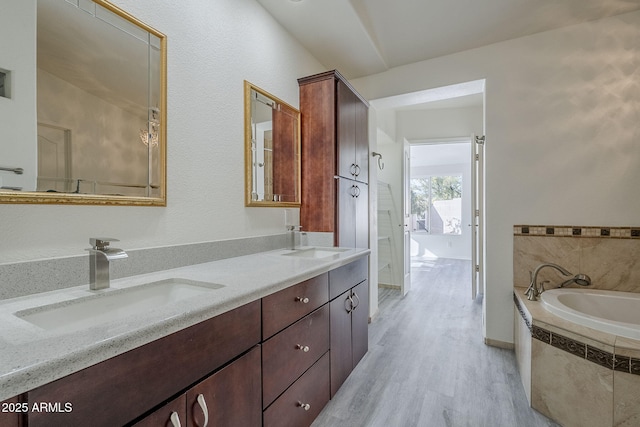 full bathroom with a garden tub, wood finished floors, double vanity, and a sink