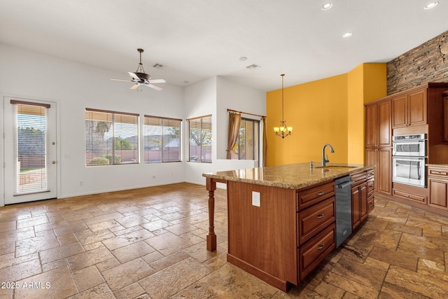 kitchen featuring a kitchen bar, sink, light stone counters, double oven, and an island with sink