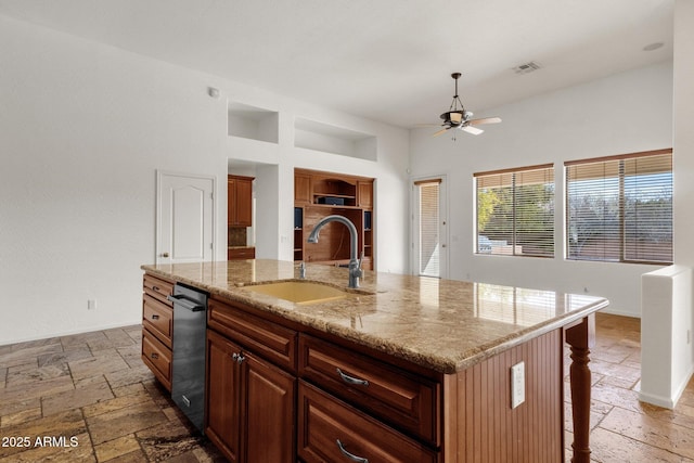 kitchen featuring a breakfast bar, sink, ceiling fan, light stone counters, and a center island with sink