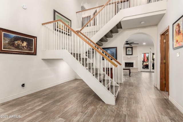 staircase with a towering ceiling, hardwood / wood-style floors, and ceiling fan