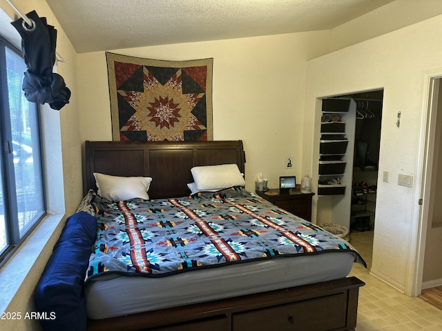 bedroom with a closet, lofted ceiling, a walk in closet, and a textured ceiling