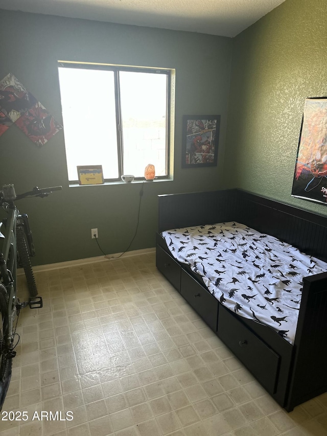 bedroom featuring a textured wall, light floors, and baseboards