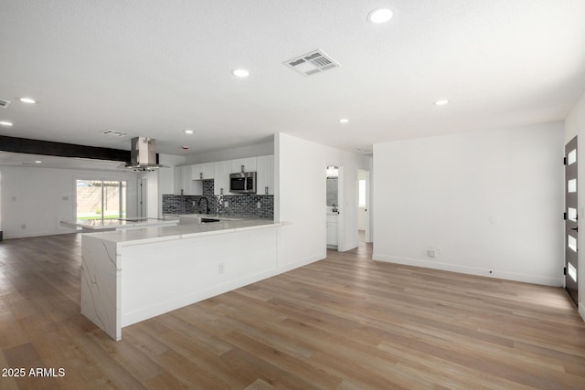kitchen featuring stainless steel microwave, exhaust hood, light wood-style floors, visible vents, and open floor plan