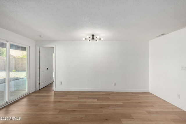 spare room featuring an inviting chandelier, light wood-style floors, visible vents, and baseboards