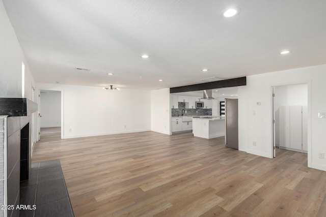 unfurnished living room featuring recessed lighting, a tile fireplace, light wood-style flooring, and baseboards