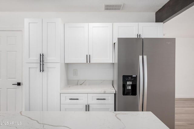 kitchen with light stone counters, white cabinets, visible vents, wood finished floors, and stainless steel fridge