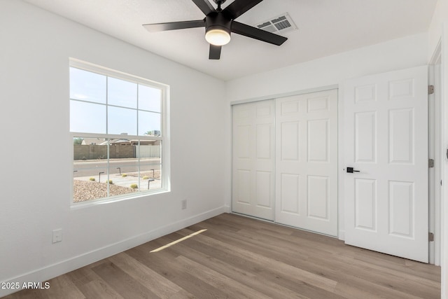 unfurnished bedroom featuring a closet, ceiling fan, visible vents, baseboards, and wood finished floors