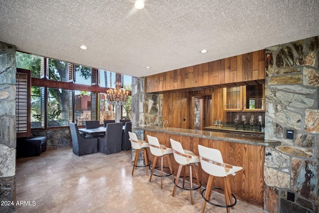 kitchen with kitchen peninsula, wood walls, dark stone counters, and a textured ceiling