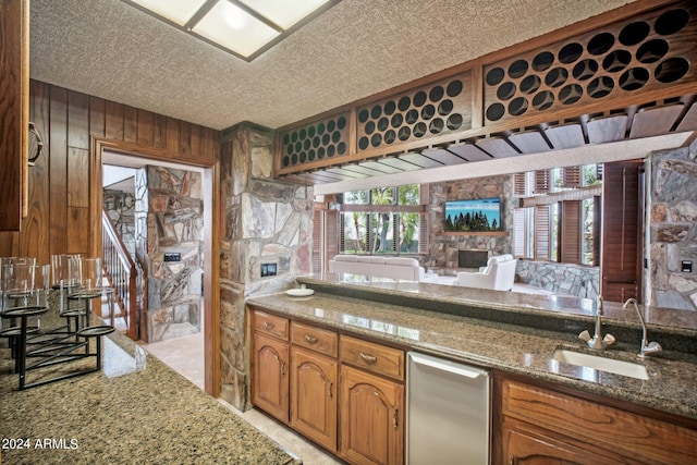 kitchen featuring a textured ceiling, wooden walls, sink, stone counters, and a fireplace