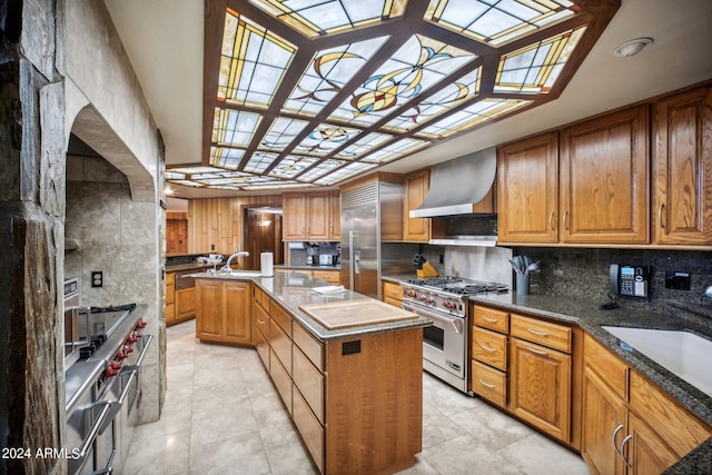 kitchen with high quality appliances, backsplash, sink, wall chimney exhaust hood, and a kitchen island