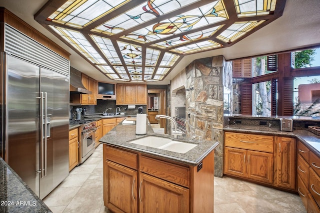 kitchen featuring decorative backsplash, high end appliances, sink, a center island with sink, and dark stone countertops