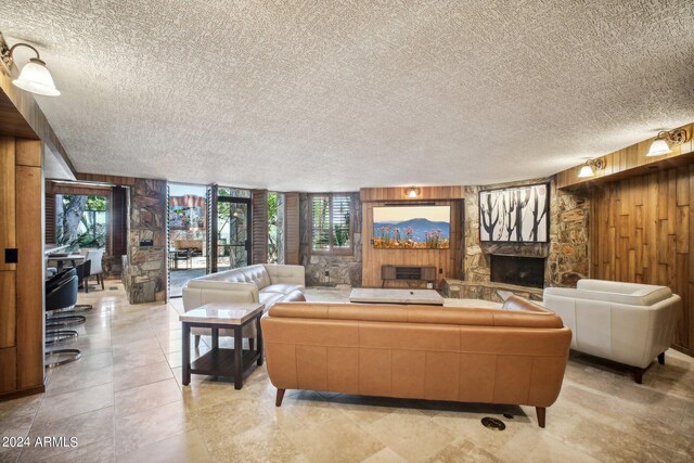 living room with a stone fireplace, a textured ceiling, and wooden walls