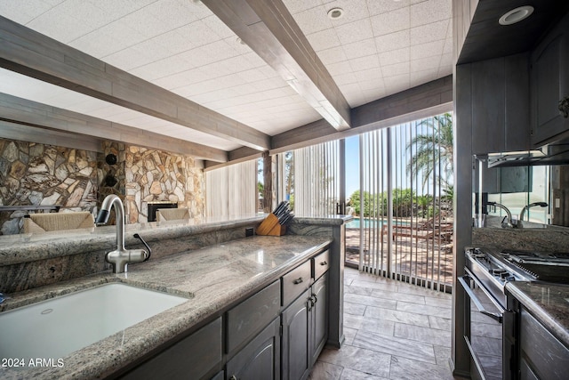 kitchen featuring beamed ceiling, high end stainless steel range, dark stone counters, and sink