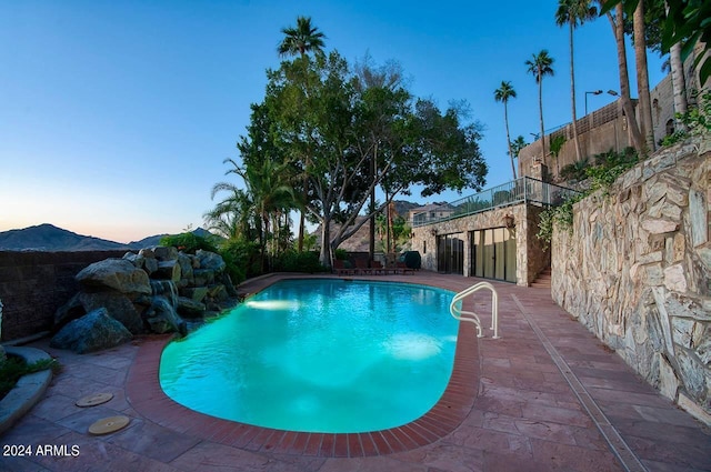 pool at dusk featuring a mountain view, pool water feature, and a patio area