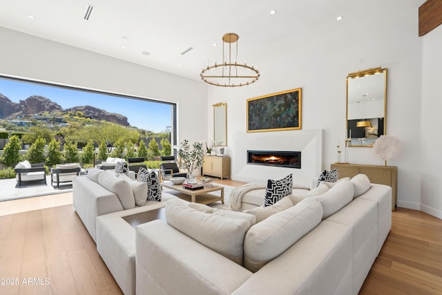 living room featuring recessed lighting, an inviting chandelier, a glass covered fireplace, and wood finished floors
