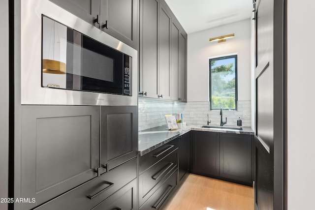 kitchen featuring stone countertops, stainless steel microwave, tasteful backsplash, a sink, and light wood finished floors