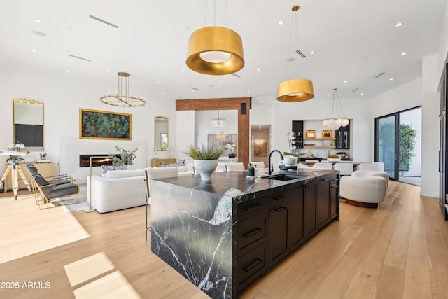 kitchen with a large island, decorative light fixtures, a sink, light wood finished floors, and open floor plan
