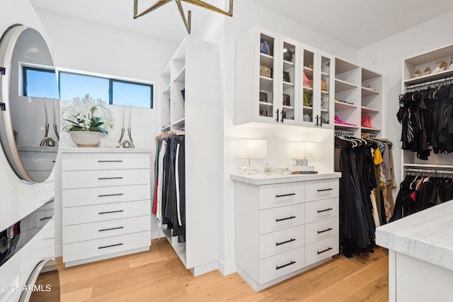 spacious closet with stacked washer / drying machine and light wood-type flooring