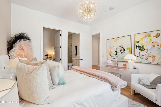 bedroom with visible vents, connected bathroom, wood finished floors, and a notable chandelier