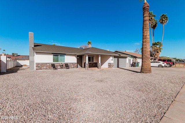 single story home with stucco siding, an attached garage, fence, stone siding, and driveway