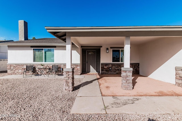 doorway to property with stone siding, a chimney, a patio area, and stucco siding