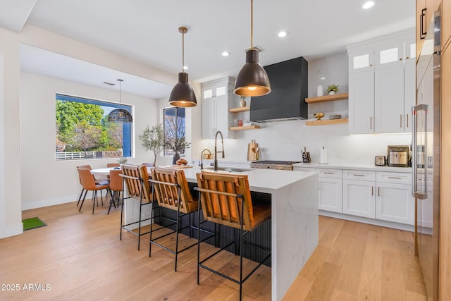 kitchen with sink, white cabinetry, decorative light fixtures, ventilation hood, and a kitchen island with sink