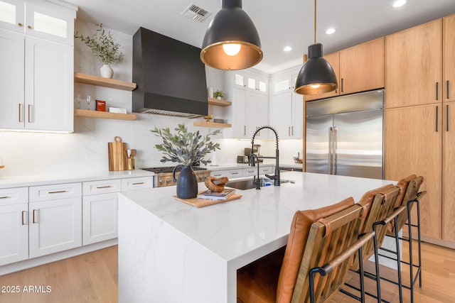 kitchen with stainless steel built in fridge, a kitchen island with sink, and white cabinets