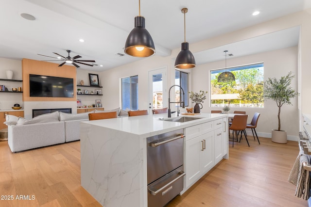 kitchen featuring sink, light stone counters, a center island with sink, pendant lighting, and white cabinets