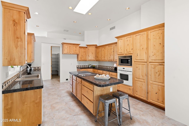kitchen with visible vents, a sink, stainless steel microwave, a kitchen island, and white oven