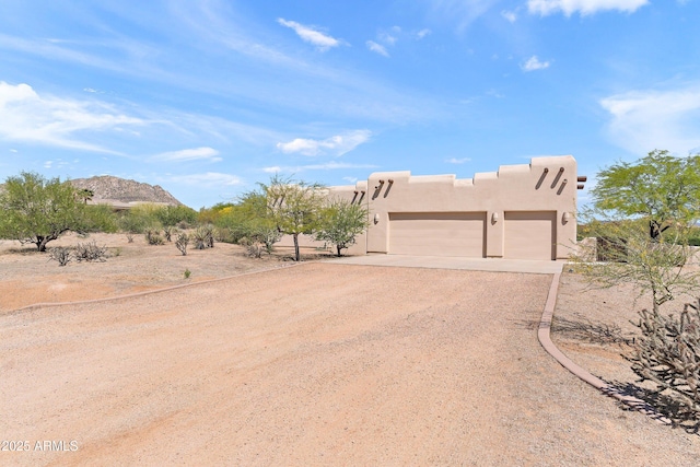 pueblo-style house with stucco siding, an attached garage, a mountain view, and dirt driveway