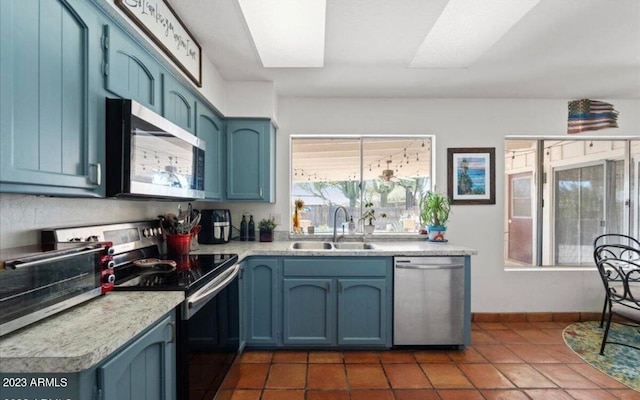 kitchen with appliances with stainless steel finishes, dark tile patterned flooring, blue cabinetry, a skylight, and sink