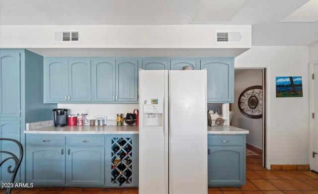 kitchen with blue cabinets, white fridge with ice dispenser, and light tile patterned floors