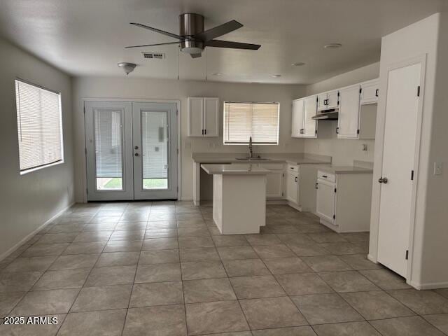 kitchen with french doors, white cabinetry, a kitchen island, a sink, and under cabinet range hood