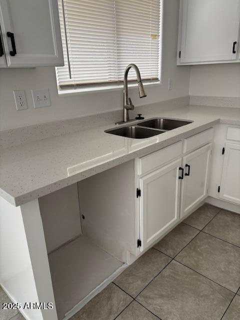 kitchen with light stone countertops, light tile patterned floors, white cabinets, and a sink