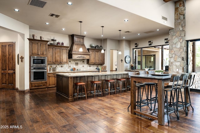 4610 E Meadowview Dr, Gilbert, AZ 85298 - kitchen featuring appliances with stainless steel finishes, custom exhaust hood, dark wood-style flooring, tasteful backsplash, and a breakfast bar area