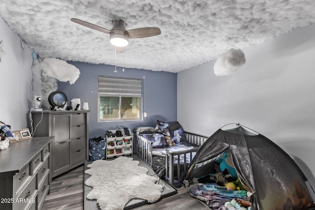 bedroom featuring a crib, ceiling fan, and dark wood-type flooring