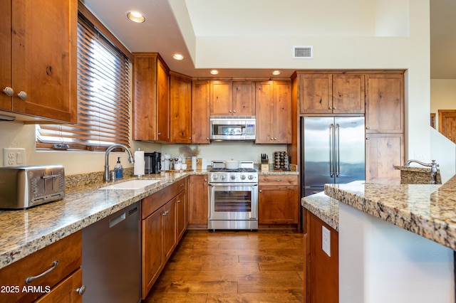 kitchen with light stone counters, dark wood-type flooring, sink, and premium appliances