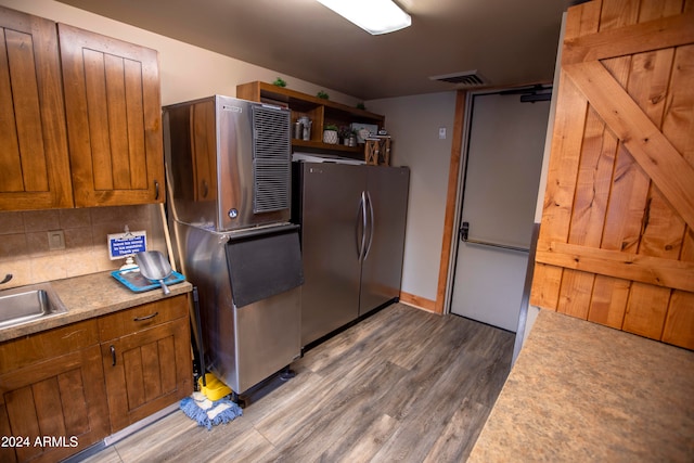 kitchen featuring sink, decorative backsplash, hardwood / wood-style flooring, and stainless steel refrigerator