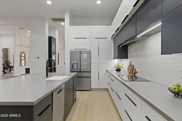 kitchen with white cabinetry, sink, stainless steel refrigerator with ice dispenser, a center island with sink, and black electric cooktop