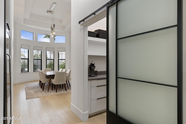 dining room with a tray ceiling, a barn door, and light hardwood / wood-style floors