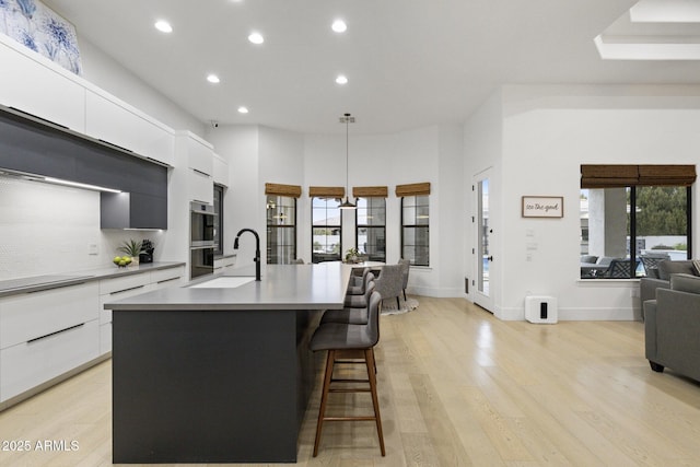 kitchen featuring sink, light hardwood / wood-style flooring, a center island with sink, pendant lighting, and white cabinets