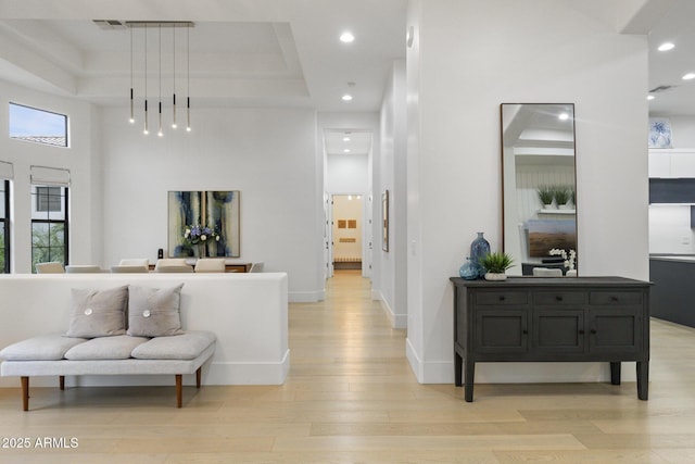 hallway with a tray ceiling, light hardwood / wood-style flooring, and a high ceiling