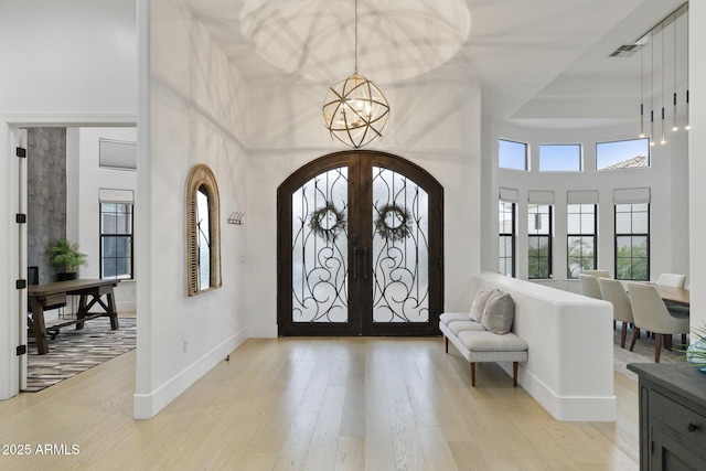 entryway featuring french doors, a towering ceiling, a notable chandelier, and light hardwood / wood-style flooring