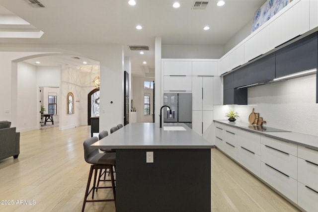 kitchen with a kitchen island with sink, sink, white cabinetry, and stainless steel fridge