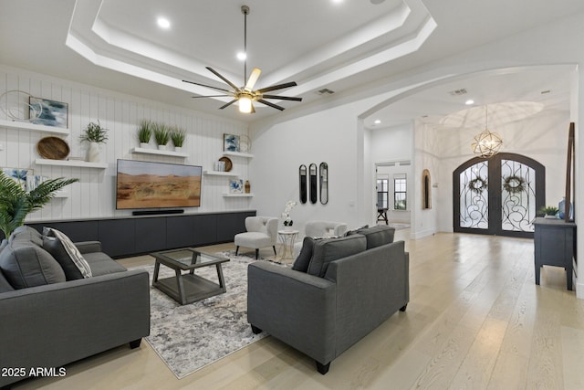 living room with a raised ceiling, light wood-type flooring, and french doors