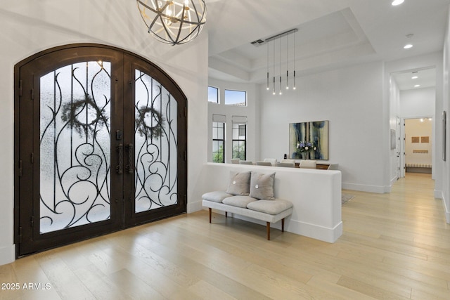 foyer entrance featuring light hardwood / wood-style flooring, a high ceiling, a raised ceiling, french doors, and a chandelier