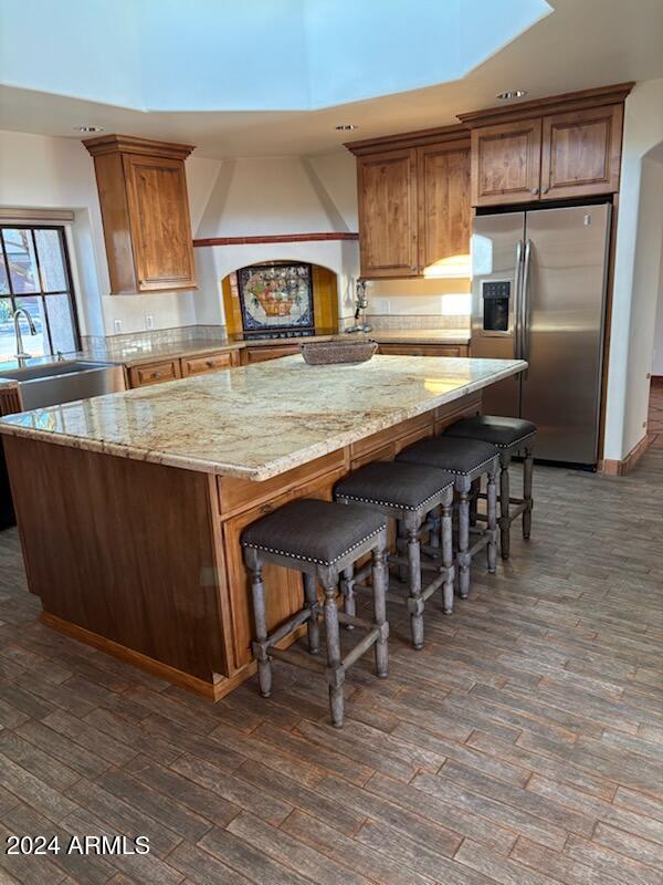 kitchen with custom exhaust hood, kitchen peninsula, dark hardwood / wood-style floors, stainless steel refrigerator with ice dispenser, and sink