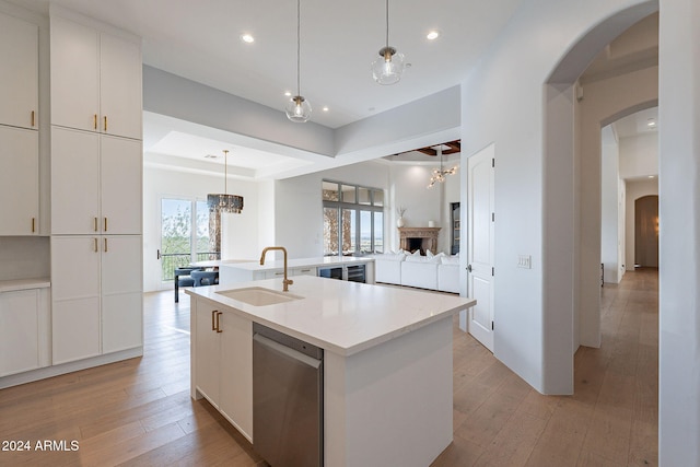 kitchen featuring light wood-type flooring, a kitchen island with sink, sink, dishwasher, and hanging light fixtures