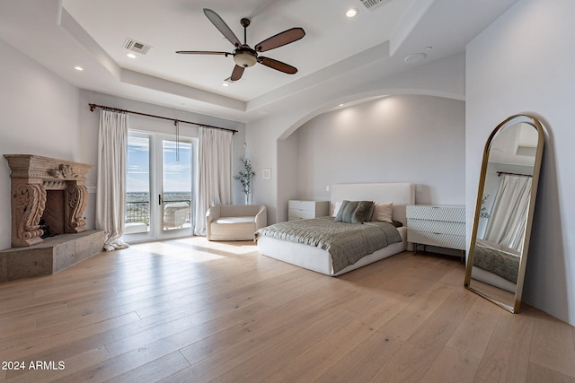 bedroom with light wood-type flooring, access to outside, a raised ceiling, and ceiling fan